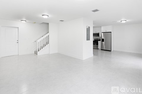 A spacious, empty room with a staircase and a kitchen area in the background.
