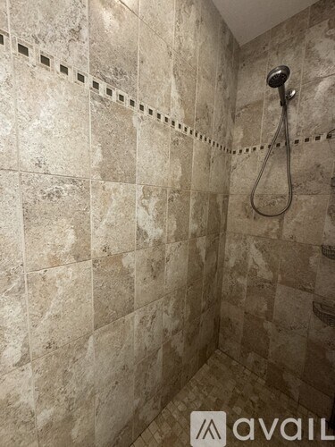 A shower with a tile wall and a hose.