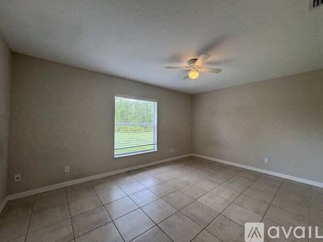 A room with a ceiling fan and a window overlooking a green area.