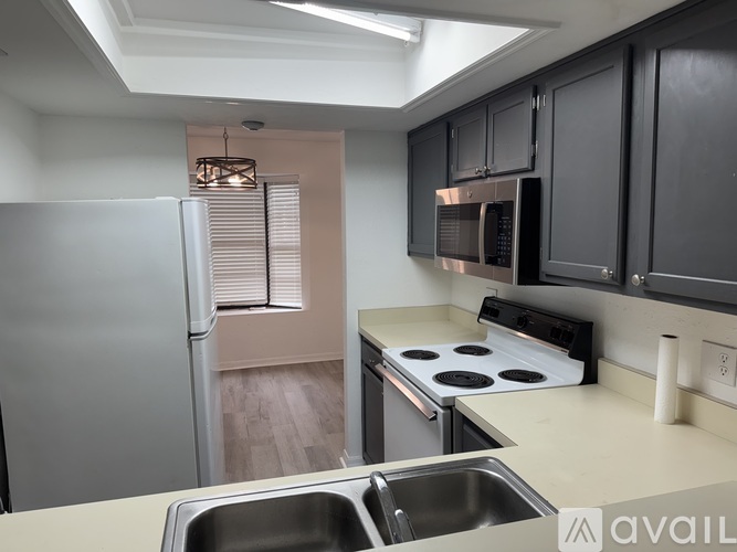 A kitchen with a stainless steel refrigerator, black cabinets, and a stove top oven.
