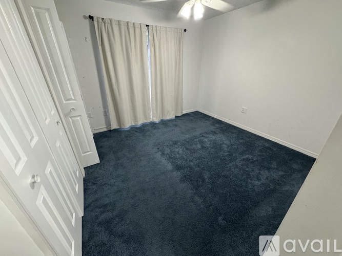 A room with a carpeted floor and a window with curtains.