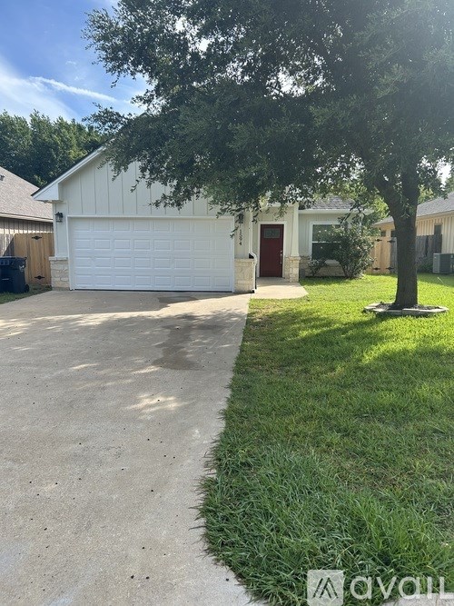 A white garage with a red door is surrounded by a green lawn and a tree.