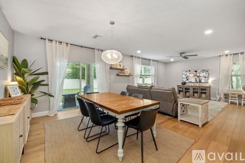 A well-lit, spacious living room with a dining table and chairs, a sofa, and a kitchen area with wooden cabinets.