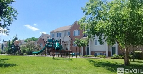 A playground with a green slide and a wooden bench in front of a building.