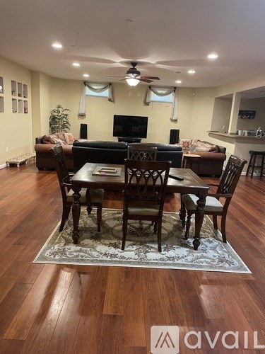 A living room with a wooden floor and a rug in front of a table with chairs.