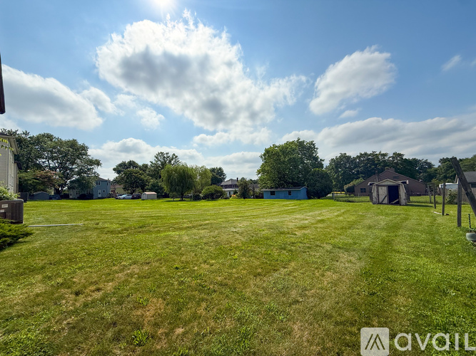 A grassy field with a few buildings in the distance under a blue sky with clouds.