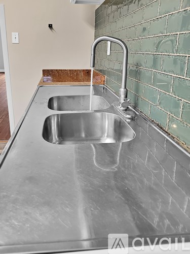 A stainless steel sink in a kitchen with green tiled walls.