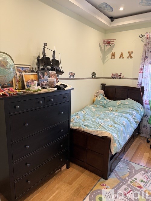A child's bedroom with a black dresser and a bed with a blue and white bedsheet.