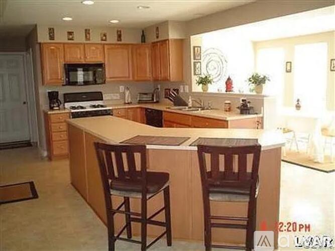 A kitchen with wooden cabinets and a countertop with two chairs.