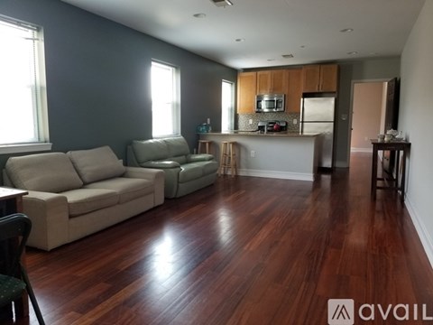 A living room with a couch, chair, and a kitchen area in the background.