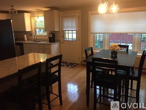 A kitchen with a table and chairs in the foreground and a window with blinds in the background.