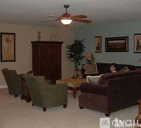 A woman is sitting on a couch in a living room with a fan on the ceiling.