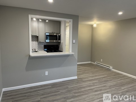 A kitchen area with a microwave and oven is visible through a window in a room with grey walls and wooden flooring.