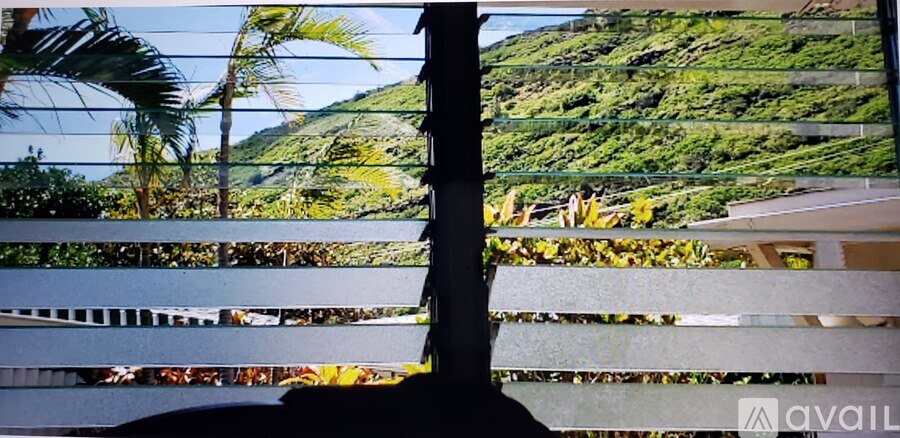A view of a hill with trees and a building in the distance through a window.