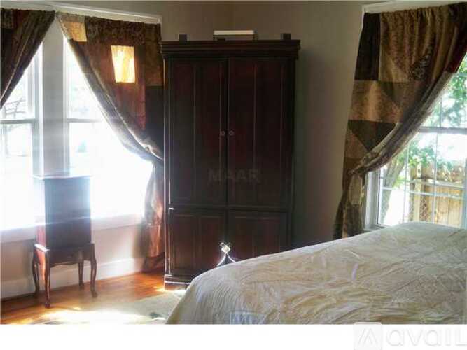 A bedroom with a large bed, a wooden wardrobe, and a chair by the window.