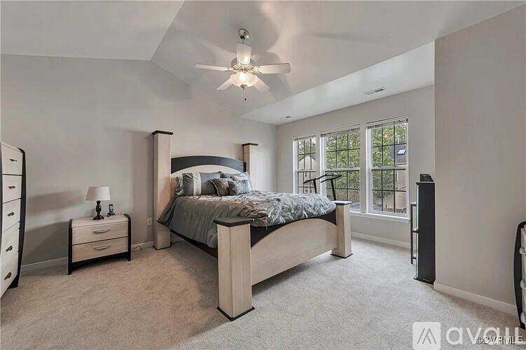 A bedroom with a large bed, a ceiling fan, and a window with a view of trees.