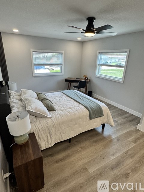 A bedroom with a bed, a ceiling fan, and a small table with a lamp on it.