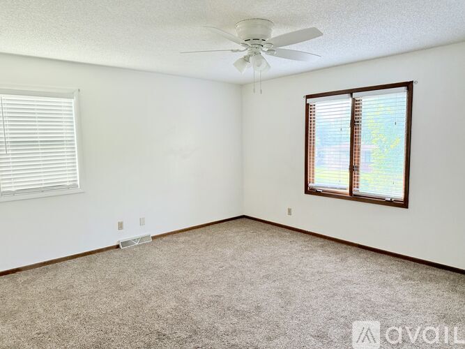 A room with a carpeted floor, a ceiling fan, and a window with blinds.
