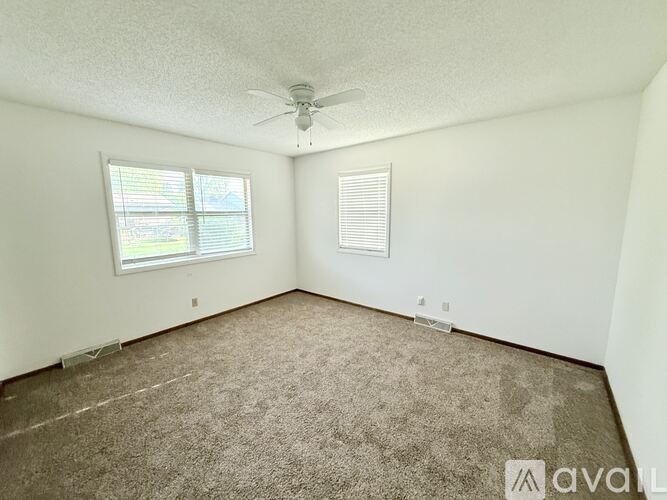 A room with a carpeted floor, a ceiling fan, and a window with blinds.