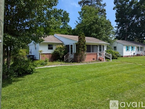 A grassy area in front of a house with a tree and a fence.
