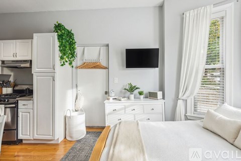 A white kitchen with a refrigerator, stove, and a TV mounted on the wall.