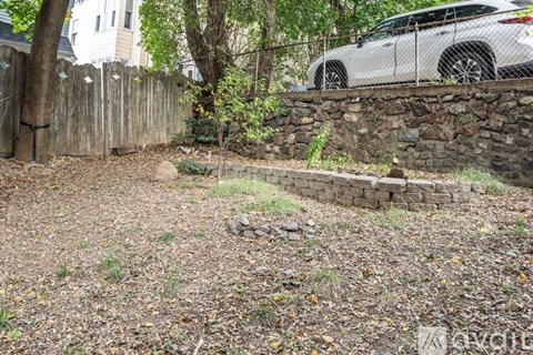 A white car is parked behind a stone wall in a backyard.