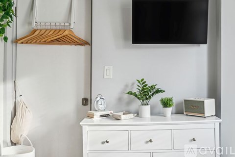 A white dresser with a wooden hanger and a white toaster on top.