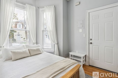 A bedroom with a large bed and a window with white curtains.