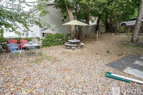 A backyard with a picnic table and chairs under a tree.