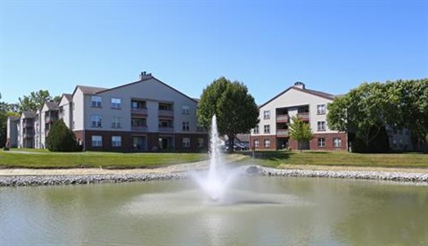 A fountain in the middle of a pond in front of apartment buildings.
