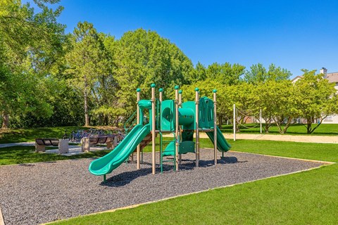 A playground with a green slide and a gravel area in the foreground.