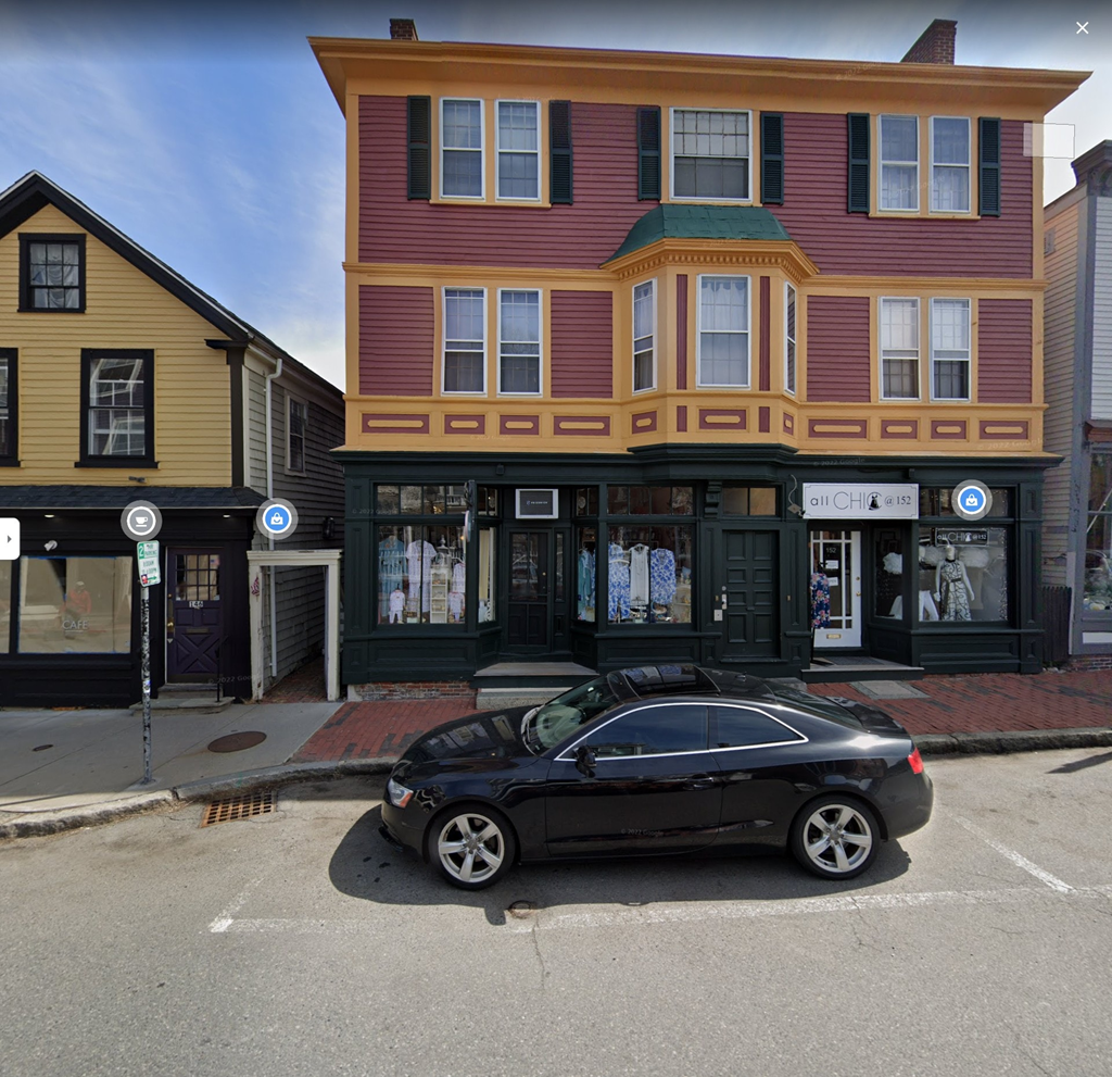 A black car is parked in front of a building with a red and yellow facade.