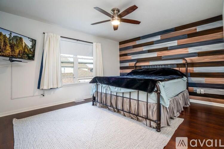 A bedroom with a bed, a ceiling fan, and a wall with wooden planks.