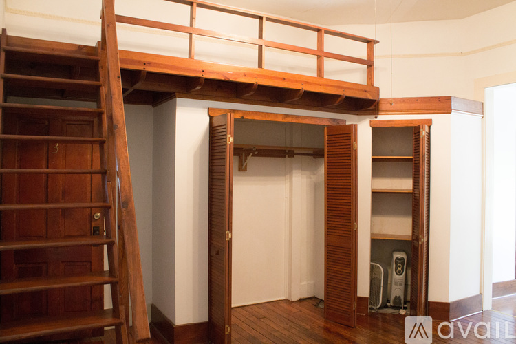 A wooden staircase with a railing is in the foreground of a room with white walls and a doorway leading to another room.