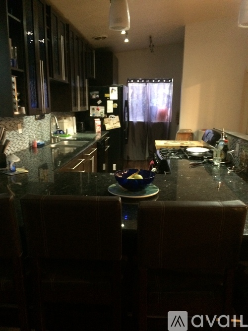 A kitchen with a granite countertop and dark brown chairs.