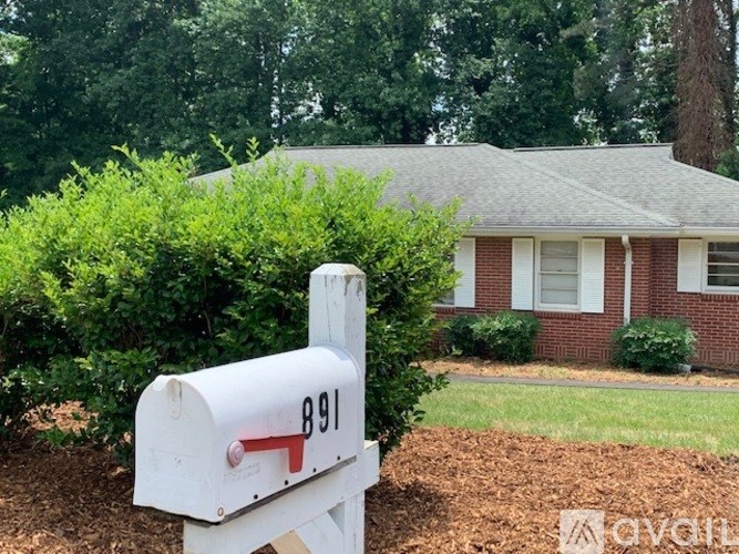 A white mailbox with the number 891 on it is in front of a house.