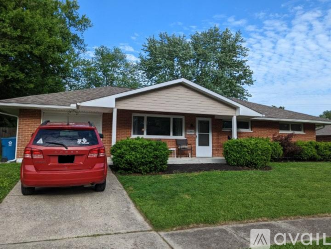 A red car is parked in front of a house with a driveway.