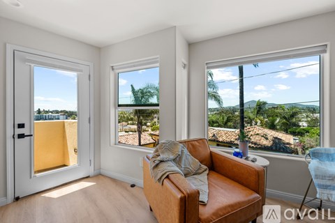 A living room with a brown leather couch and a view of the outdoors through the windows.