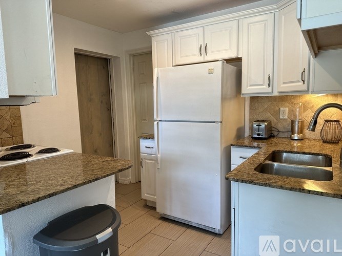 A kitchen with a white refrigerator, a countertop, and a trash can.