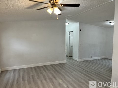A room with a ceiling fan and light fixture, and a door in the background.