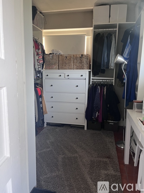 A small, neatly organized bedroom with a white dresser and a closet with clothes.