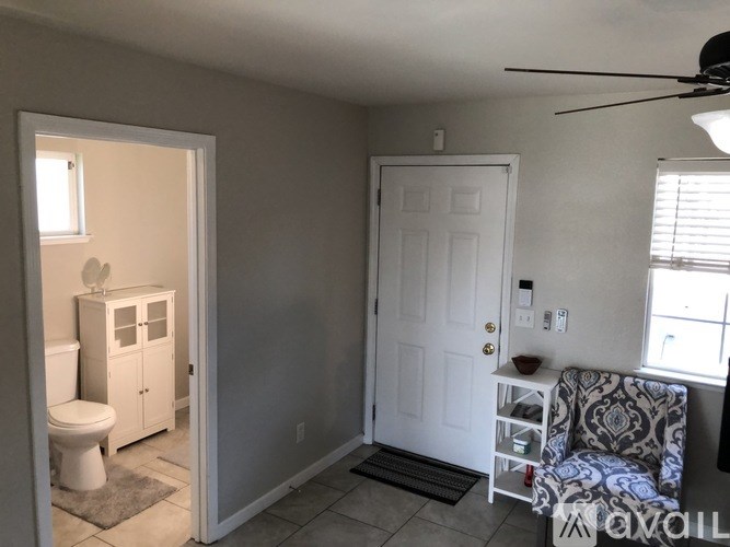 A small room with a toilet, a cabinet, a chair and a fan.