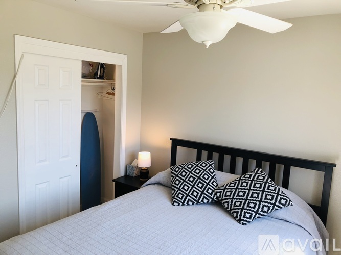 A bedroom with a bed, pillows, a ceiling fan, and a nightstand with a lamp.
