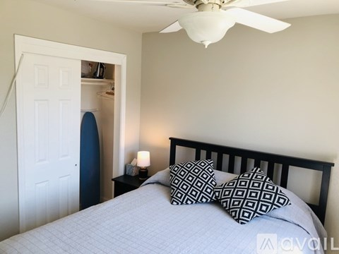 A bedroom with a bed, pillows, a ceiling fan, and a nightstand with a lamp.