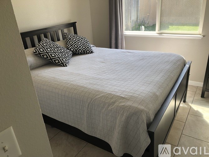 A bed with a grey comforter and two pillows with a black and white pattern.
