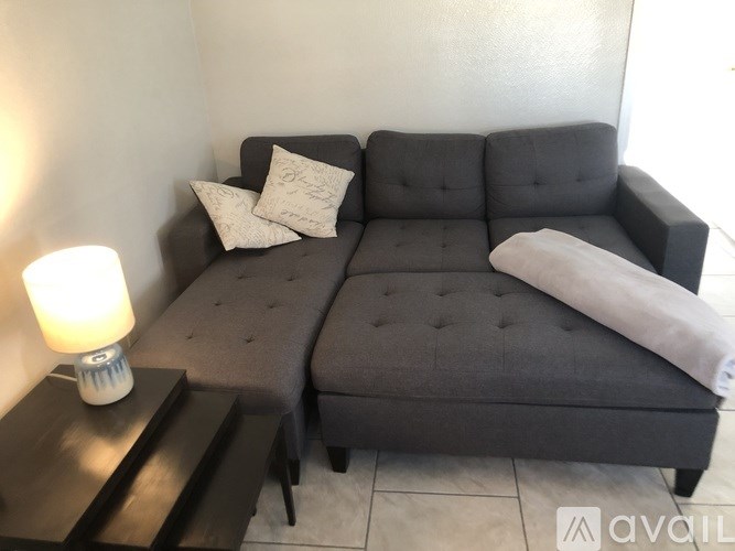 A grey couch with a white pillow and a white blanket on it.