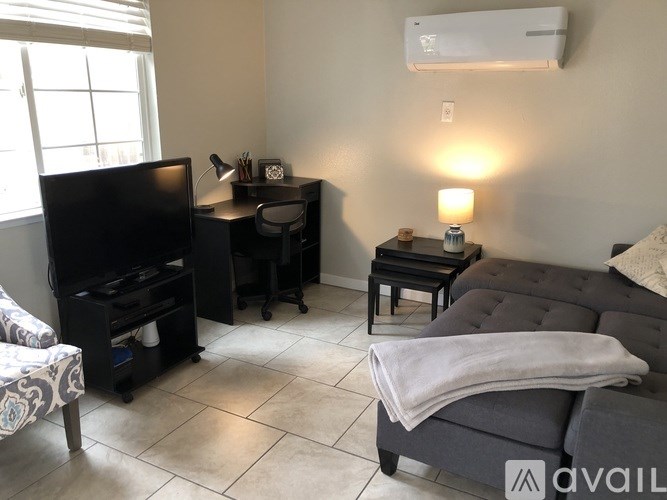 A living room with a grey couch, a black desk, and a black chair.