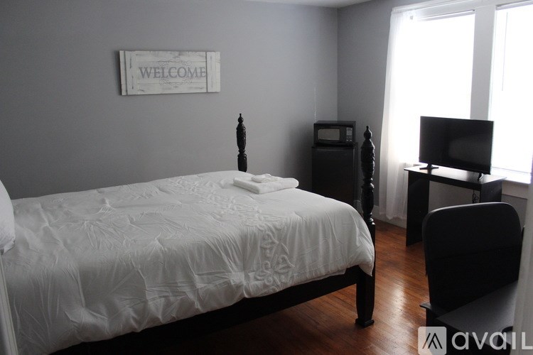 A bedroom with a bed, chair, and a welcome sign on the wall.
