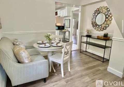 A living room with a white sofa, a small table with a vase of flowers, and a mirror on the wall.