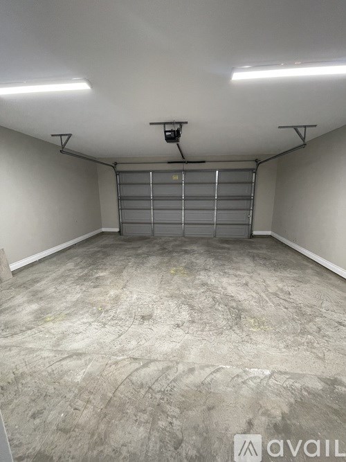 A large, empty room with a concrete floor and a metal rolling shutter on the back wall.